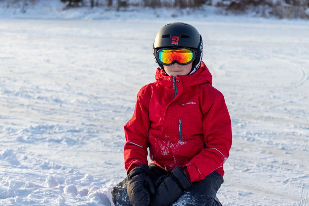 boy in ski goggles and helmet sits in the snow