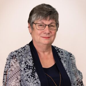 Warden Eleanor Roulston, a smiling woman with light skin, dark grey hair, hazel eyes, and glasses